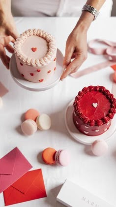 a woman is decorating a cake with red icing and hearts on the top