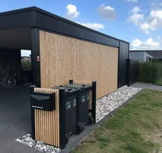 two black trash cans sitting in front of a building with wood panels on the side