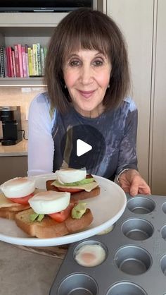 a woman sitting at a table with a plate of food in front of her and muffin tins on the counter