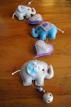 three small stuffed elephants on a wooden table with beaded hearts hanging from the strings