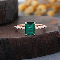 an emerald and diamond ring sitting on top of a piece of wood