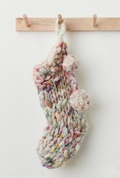 a knitted stocking hanging from a wooden hanger on a white wall with pegs