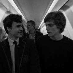 black and white photograph of two men walking down an escalator with other people in the background