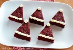 four pieces of red velvet cake with white frosting on top, sitting on a plate