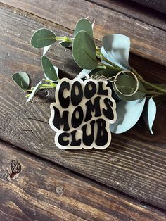 a keychain that says cool mom's club on it next to some leaves