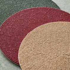 three woven place mats sitting on top of each other in different colors and sizes,