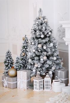 a christmas tree with silver and white ornaments in front of two small presents on the floor