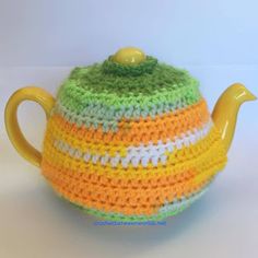 a crocheted tea pot cover with a yellow handle and green, white, and orange stripes