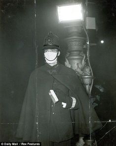 black and white photograph of a man wearing a hat, cape and gloves standing in front of a lamp post