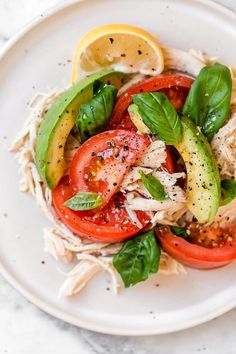 a white plate topped with chicken, tomatoes and cucumber slices on top of pasta