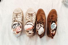 three pairs of shoes are lined up on a white surface, one is open and the other has folded clothes