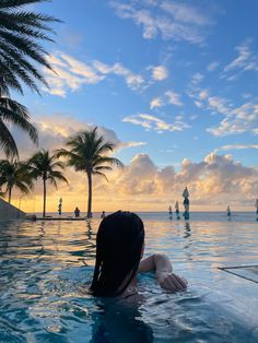 a woman sitting in the middle of a swimming pool with palm trees and sailboats in the background