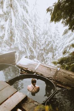 a woman sitting in a hot tub surrounded by snow covered trees and evergreens on the mountain