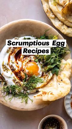 an egg and some herbs in a bowl on a table next to pita bread