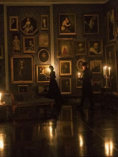 two people standing next to each other in a room with pictures on the wall and candles lit