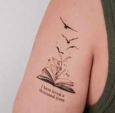 a woman's arm with a book and birds tattoo on it that says i have lived a thousand lives