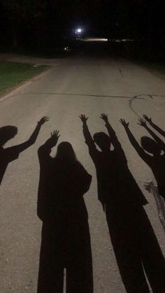 the shadow of several people reaching up in the air with their hands, on a street at night