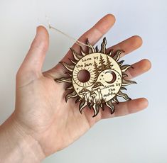 a hand holding a wooden sun and moon ornament