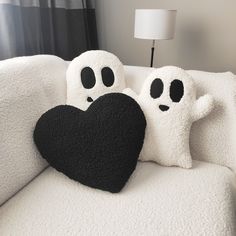 two stuffed ghost pillows sitting on top of a white couch next to a black heart