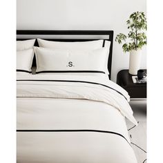 a bed with white sheets and black trimmings in a room next to a potted plant