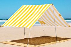 a yellow and white striped tent sitting on top of a sandy beach