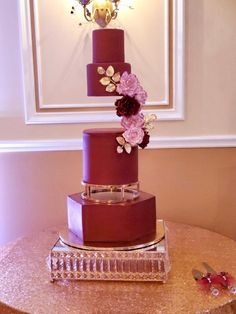 a three tiered cake with purple flowers on top sits on a table in front of a mirror