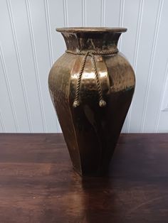 a gold colored vase sitting on top of a wooden table next to a white wall