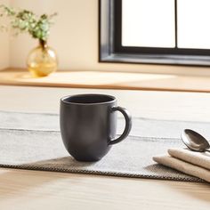 a black coffee cup sitting on top of a table next to two silver spoons