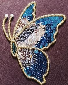 a blue and white butterfly with sequins on it's wings is sitting on a purple cloth