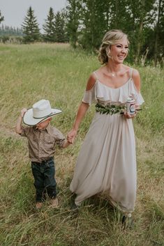 a woman in a dress holding the hand of a young boy wearing a cowboy hat