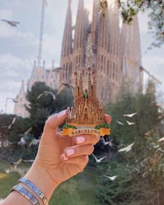 a hand holding up a miniature model of barcelona, spain in front of the saffroni tower