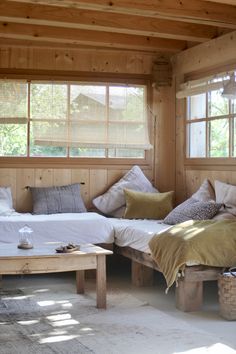 two beds in a room with wooden walls and windows, one is made from wood