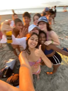 a group of young people standing on top of a beach next to the ocean giving thumbs up