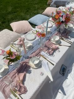 the table is set with plates, silverware and pink flowers in vases on it