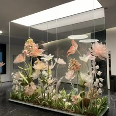 an arrangement of flowers is displayed in front of a glass display case with mirrors on the wall