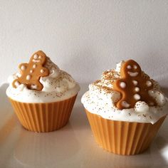 two cupcakes with white frosting and gingerbread decorations on top, sitting on a plate