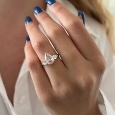 a woman's hand wearing a ring with two pear shaped diamonds on it and blue fingernails