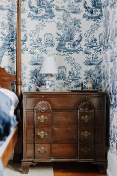 a bed sitting next to a wooden dresser in a room with blue and white wallpaper