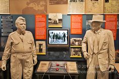 two statues of men standing next to each other in front of a wall with pictures on it