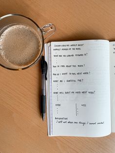 an open book next to a cup of coffee and a pen on a wooden table