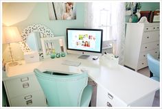 a white desk topped with a computer monitor next to a blue chair and dresser under a window