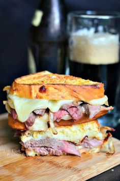 a sandwich cut in half sitting on top of a cutting board next to a glass of beer