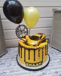 a birthday cake with a yellow car and black balloons on the top is for an automobile enthusiast