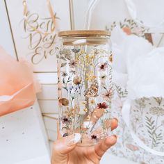 a person holding a glass with flowers painted on it and a straw in their hand