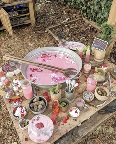 a wooden table topped with lots of dishes and bowls filled with pink liquid next to plants