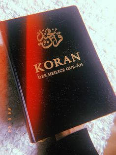 a close up of a person's hand holding an open koran book on the ground