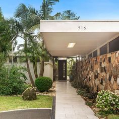 the entrance to a home with stone walls and palm trees in the front lawn area