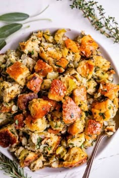 a white plate topped with stuffing next to a fork and sprig of rosemary