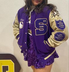 a woman wearing a purple and gold jacket with sequins on the bottom, standing in front of a wall