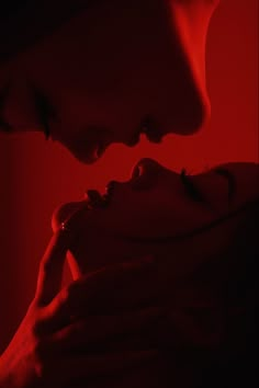 a woman holding a man in the dark with red light behind her and blood dripping on his face